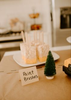 there is a small christmas tree on the table with marshmallows and paint brushes