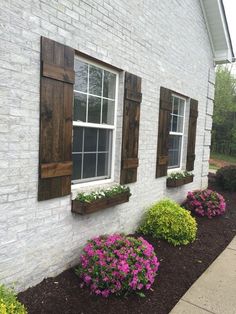 a white brick house with wooden shutters and flowers in the window boxes on each side