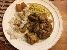 a white plate topped with meat, rice and corn on top of a wooden table