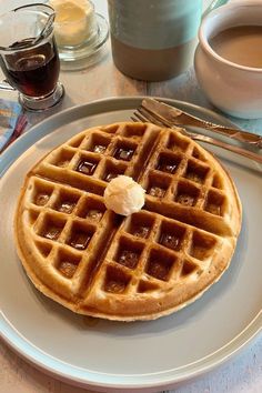 a waffle on a plate next to a cup of coffee and some silverware