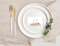 a white plate topped with a fork and knife next to a paper place card on top of a table