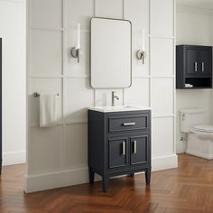 a bathroom with white walls and wood flooring has a sink, mirror, toilet and cabinets