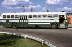 an old green and white bus is parked on the side of the road