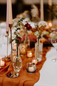 a table with candles and vases filled with flowers on it's side, along with other place settings