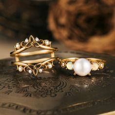 two rings sitting on top of a book next to each other, one with a pearl in the middle