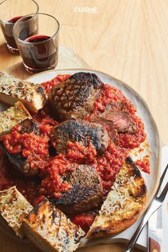 a white plate topped with meat covered in marinara sauce next to two glasses of wine