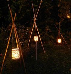 some lights are lit up in the dark by poles and jars with candles inside them