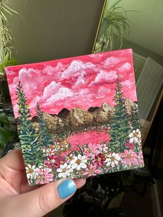 a hand holding up a small card with mountains in the background and flowers on it