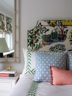 a white bed topped with lots of pillows next to a wall mounted mirror and lamp