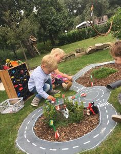 two young boys playing with toy cars in the grass on a miniature road and track