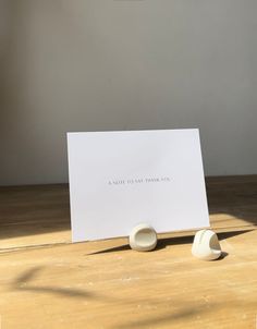 two small white bowls sitting on top of a wooden table next to a card that says,