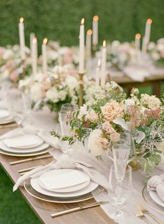 the table is set with white plates and silverware, candles and flowers in vases