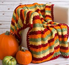 a crocheted blanket sitting on top of a chair next to two pumpkins