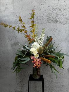 a vase filled with lots of flowers on top of a black stand next to a wall