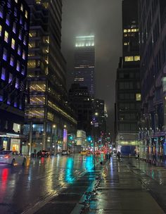 a city street at night with cars driving on the road and tall buildings in the background