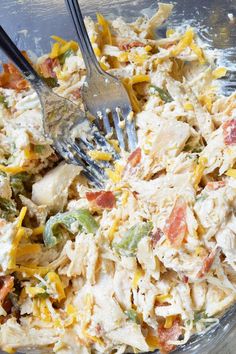 a glass bowl filled with chicken salad and two plastic forks in it's center