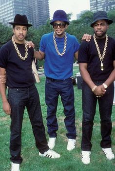 three men standing in the grass with one wearing a black hat and two wearing blue