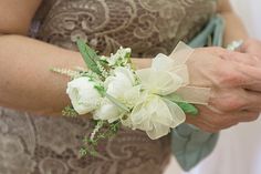 a woman in a brown dress holding a bouquet of white flowers and greenery on her arm