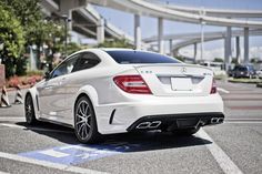 the rear end of a white car parked in a parking lot next to an overpass