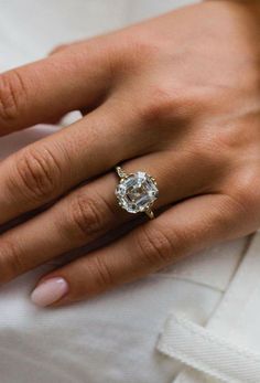 a woman's hand with a diamond ring on her left hand, wearing a white shirt