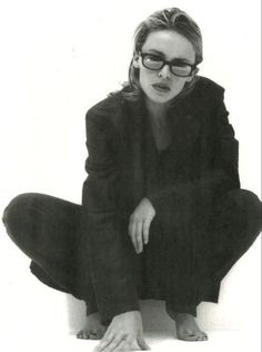 a black and white photo of a woman in glasses sitting on the ground with her legs crossed