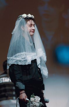 a man wearing a veil and holding a bouquet in his hand while walking down the runway