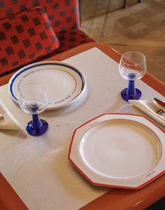 the table is set with two plates, silverware and wine glasses on it's placemats