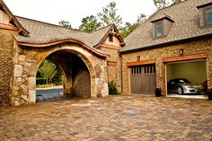 a car is parked in front of a brick house with two garages and an arched doorway