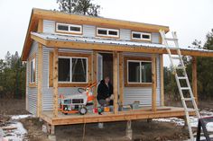 a man standing in the doorway of a tiny house with windows and siding on it