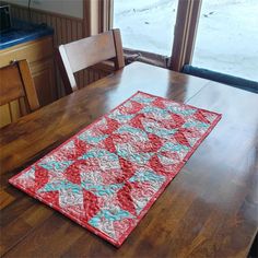 a red and blue table runner on top of a wooden table next to a window