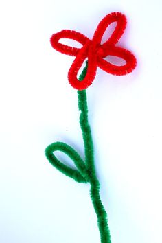 a red flower with green stems sitting on top of a white table next to a piece of string