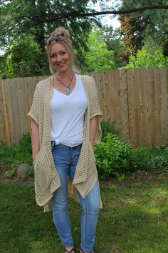 a woman standing in front of a fence wearing jeans and a white shirt with a crocheted cardigan