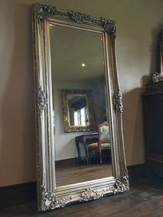 a large silver framed mirror sitting on top of a wooden floor next to a table