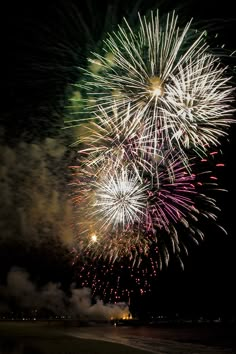 fireworks are lit up in the night sky over water and beach area with dark skies