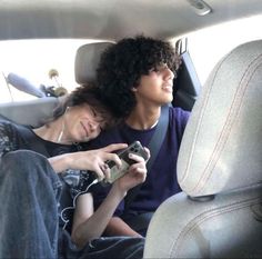 a man and woman sitting in the back seat of a car, one holding a camera