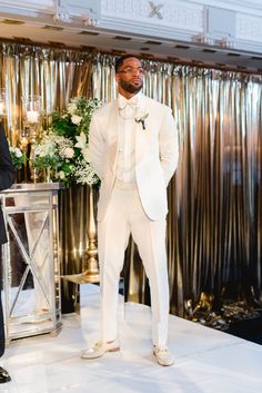 a man in a white tuxedo standing next to another man wearing a suit