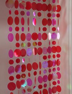 a red and pink mobile with circles hanging from it's sides in front of a window