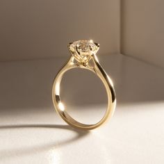 a yellow gold engagement ring with an oval shaped diamond on the center and side, sitting on a white surface