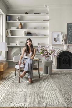 a woman sitting on a chair in front of a fire place and bookshelf