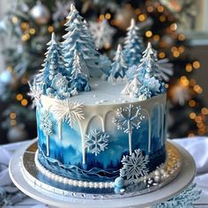 a blue and white frosted cake with snowflakes on it, surrounded by christmas trees