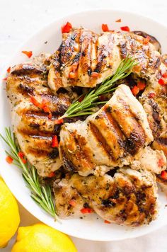 grilled chicken with rosemary garnish in a white bowl next to lemons