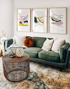 a living room with a green couch and rugs on the floor, framed pictures above it