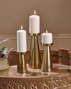 three candles sitting on top of a table next to a basket with plants in it