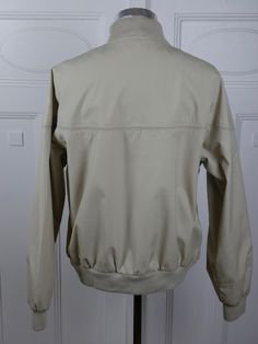 "This classic collegiate-look ivory beige jacket has a soft acrylic knit collar and ribbed cuffs and waistband. The lightweight jacket zips closed in front and closes further with two buttons on the waistband and another at the neckline. The jacket has three stainless steel airing grommets at the back of each underarm seam. Brand label: Hill & Archer (Made in China) Size: 42 to 44 US/UK Material: 65% polyester, 35% cotton Chest = 46 inches (116.84cm) (This is a Size 44 US/UK; the extra space Fitted Beige Outerwear With Ribbed Cuffs, Cream Outerwear With Ribbed Cuffs For Work, Solid Collared Outerwear With Ribbed Cuffs, Casual Beige Outerwear With Ribbed Collar, Beige Casual Outerwear With Ribbed Collar, Cream Outerwear With Ribbed Collar For Fall, Classic Beige Outerwear With Ribbed Cuffs, Long Overcoat, Beige Jacket