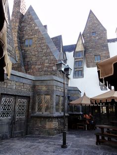 an outdoor area with tables and umbrellas in front of a castle like building that looks like it is made out of stone