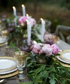 the table is set with candles, plates and flowers in gold vases on it