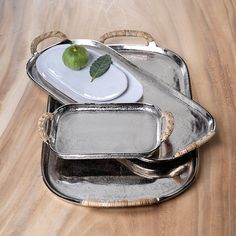 two serving trays with silverware and a green leaf on them sitting on a wooden table