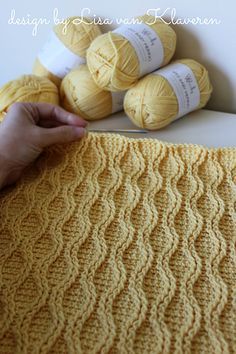 a hand holding a yellow crocheted blanket next to several balls of yarn on a table