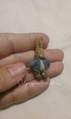 a small crocheted rabbit in a blue dress sitting on someone's hand