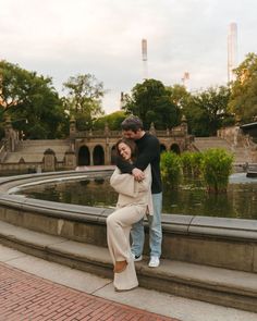 a man standing next to a woman on top of a stone wall near a pond